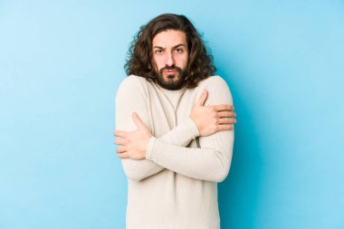 Uzun saçlı genç adam mavi bir arka planda izole edilmiş. Düşük ateş ya da hastalık yüzünden soğuyor..