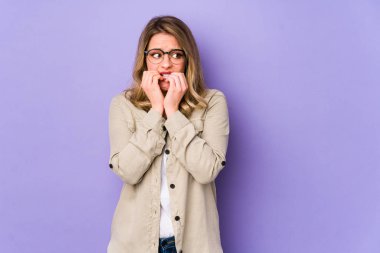 Mor arka planda izole edilmiş, tırnak yiyen, gergin ve endişeli bir beyaz kadın..