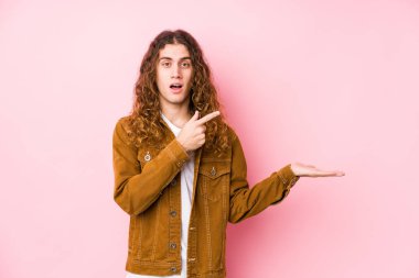 Genç, uzun saçlı adam yalnız poz veriyor. Elinde bir kopyası var..