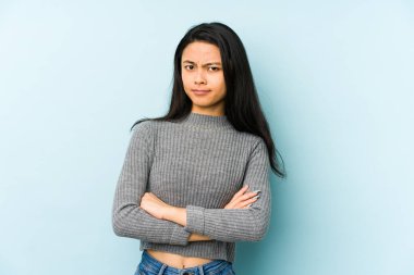 Mavi bir arka planda izole edilmiş genç Çinli kadın alaycı bir ifadeyle kameraya bakıyor..