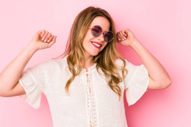 Pembe arka planda gözlüklü genç beyaz kadın özel bir günü kutluyor, atlıyor ve enerji dolu kollarını kaldırıyor..