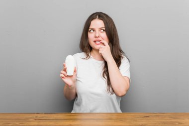 Genç ve cüsseli kadın elinde nemlendirici tutarken rahat bir şekilde fotokopi odasına bakan bir şey düşünüyor..