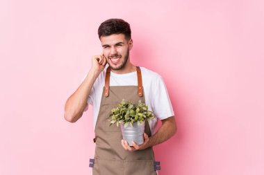 Kafkasyalı genç bahçıvan bir bitki tutuyor. Elleriyle kulaklarını kapatıyor..