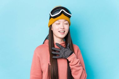 Kayak kıyafetleri giyen genç Çinli bir kadın yalnızken kahkahalar atıyor ve elini göğsüne koyuyor..