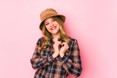 Kafkasyalı şapkalı genç bir kadın izole edilmiş gülümsüyor ve elleriyle kalp şeklini gösteriyor..