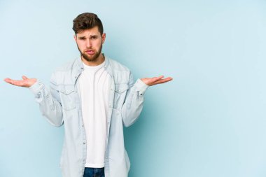 Kafkasyalı genç adam mavi arka planda izole edilmiş. Kafası karışmış ve omuz silkiyor. Kopya alanını tutmak için..