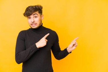 Sarı arka planda izole edilmiş genç bir Arap adam işaret parmağıyla fotokopi alanını işaret ederek şok oldu..