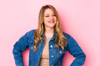 Pembe arka planda izole edilmiş beyaz bir kadın. Kendine güveni tam. Kalçalarını tutuyor..