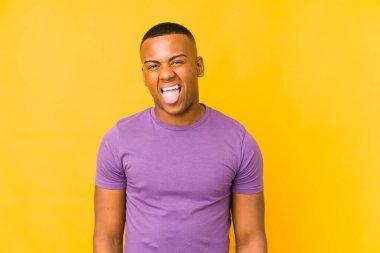 Sarı arka planda izole edilmiş genç latin adam komik ve dost canlısı bir dil uzatıyor..