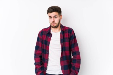 Beyaz arka planda poz veren beyaz tenli genç adam omuz silkiyor ve gözleri açık..