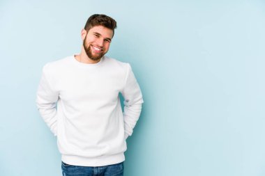 Mavi arka planda izole edilmiş genç beyaz adam mutlu, güler yüzlü ve neşeli.