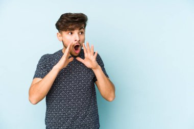 Mavi arka planda izole edilmiş genç bir Arap yüksek sesle bağırıyor, gözleri açık ve elleri gergin tutuyor..