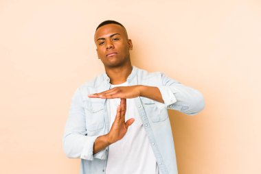 Bej arka planda izole edilmiş genç latin adam bir mola hareketi gösteriyor.