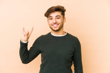 Bej arka planda izole edilmiş genç bir Arap adam boynuzlarını devrim konsepti olarak gösteriyor..