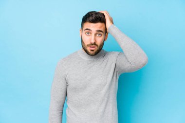 Mavi arka planda genç, beyaz bir adam izole edilmiş, yorgun ve uykulu. Elini başının üstünde tutuyor..