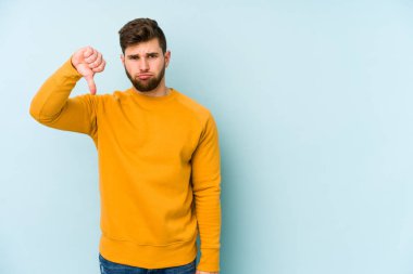 Mavi arka planda izole edilmiş genç beyaz bir adam hoşlanmadığı bir jest yapıyor. Anlaşmazlık konsepti.