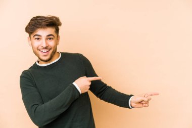 Bej bir arka planda izole edilmiş genç bir Arap işaret parmağıyla işaret ederek heyecanlanıyor..