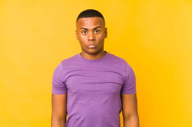 Sarı arka planda izole edilmiş genç bir latin omuz silker ve gözleri açık kalır..