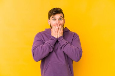 Sarı arka planda izole edilmiş genç beyaz bir adam bir şeye gülüyor, ağızlarını ellerle kapatıyor..