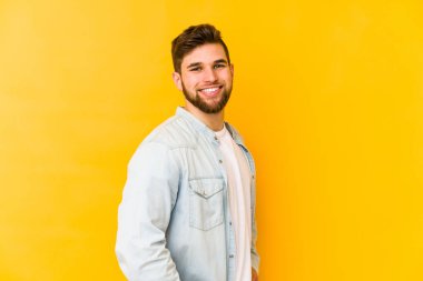 Sarı arka planda izole edilmiş genç beyaz adam ellerini kalçalarına koyuyor..