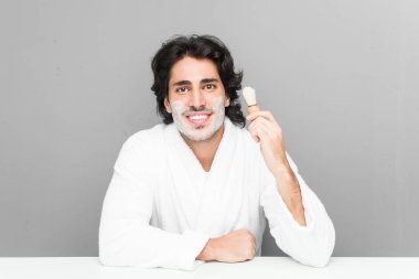 Gri bir arka planda sakalını kesen genç beyaz bir adam.