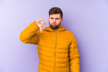 Mor arka planda izole edilmiş genç adam baş parmağını aşağı gösteriyor, hayal kırıklığı konsepti..