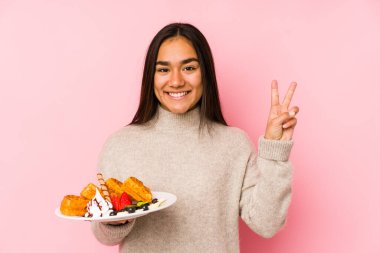 Genç Asyalı kadın waffle tutuyor. İki numarayı parmaklarıyla gösteriyor..
