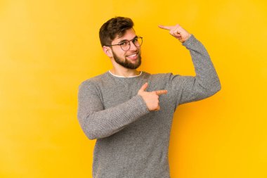 Sarı arka planda izole edilmiş genç beyaz adam işaret parmaklarıyla küçük bir şey tutuyor, gülümsüyor ve kendinden emin..