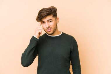 Bej arka planda izole edilmiş genç bir Arap adam işaret parmağıyla hayal kırıklığı jesti gösteriyor..