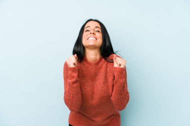 Kafkasyalı genç bir kadın mavi arka planda izole edilmiş mutlu ve başarılı hissediyordu. Zafer konsepti.