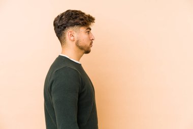 Genç Arap adam bej bir arka planda izole edilmiş, sola bakıyor, yandan poz veriyor..