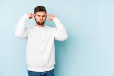 Kafkasyalı genç adam mavi arka planda izole edilmiş bir göreve odaklanmış, parmaklarını işaret ediyor..