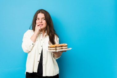 Genç, kıvrımlı bir kadın elinde keklerle rahatlamış fotokopi odasına bakan bir şey düşünüyor..