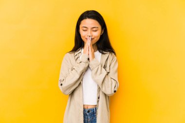 Sarı bir arka planda izole edilmiş genç Çinli bir kadın el ele tutuşup dua ederken kendine güveniyor..