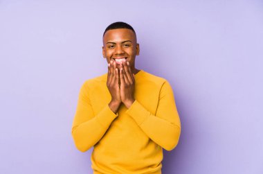 Mor arka planda izole olmuş genç Latin bir adam bir şeye gülüyor, elleriyle ağzını kapatıyor..