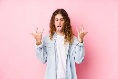 Uzun saçlı adam izole bir şekilde poz veriyor, parmaklarıyla kaya hareketi yapıyor.