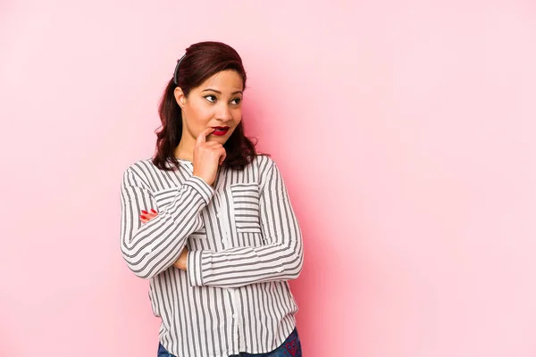 Middle age latin woman isolated on a pink background relaxed thinking about something looking at a copy space.