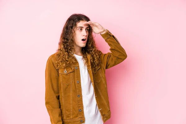 Young long hair man posing isolated looking far away keeping hand on forehead.