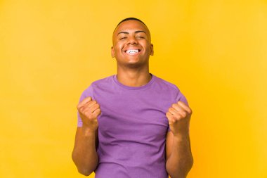 Sarı arka planda yalnız yaşayan genç latin adam tasasız ve heyecanlı bir şekilde tezahürat yapıyor. Zafer konsepti.