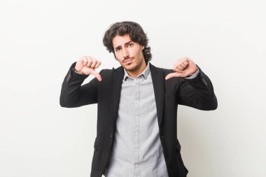 Genç bir iş adamı beyaz bir arkaplanda baş parmağını aşağı gösteriyor ve hoşlanmadığını ifade ediyor..