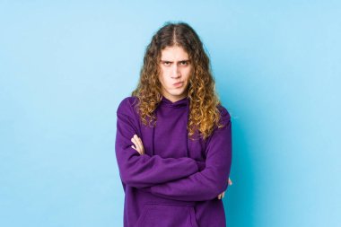 Uzun saçlı bir adam hoşnutsuzca somurtuyor, kollarını kavuşturuyor..