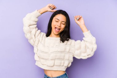 Mor arka planda izole edilmiş genç Çinli bir kadın özel bir günü kutluyor, atlıyor ve enerjiyle kollarını kaldırıyor..