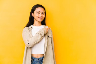 Sarı arka planda izole edilmiş genç Çinli kadın gülümsüyor ve boş alanda bir şey gösteriyor..