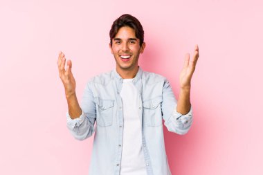 Pembe arka planda poz veren beyaz bir genç hoş bir sürprizle karşılaşıyor, heyecanlı ve el kaldırıyor..