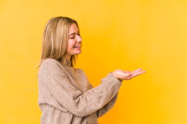 Sarışın, beyaz, sarı arka planda izole edilmiş bir kadın. Elinde palmiye ağacında bir kopya alanı var..