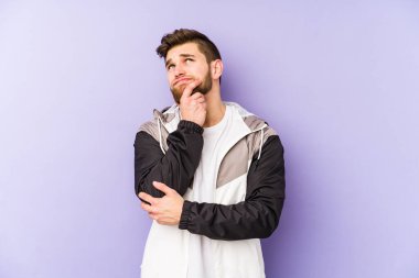 Genç adam mor arka planda izole edilmiş düşünüyor, yukarı bakıyor, yansıtıyor, düşünüyor, bir fantezi kuruyor..