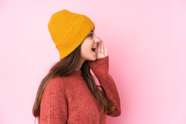 Young caucasian woman wearing a wool cap shouting and holding palm near opened mouth.