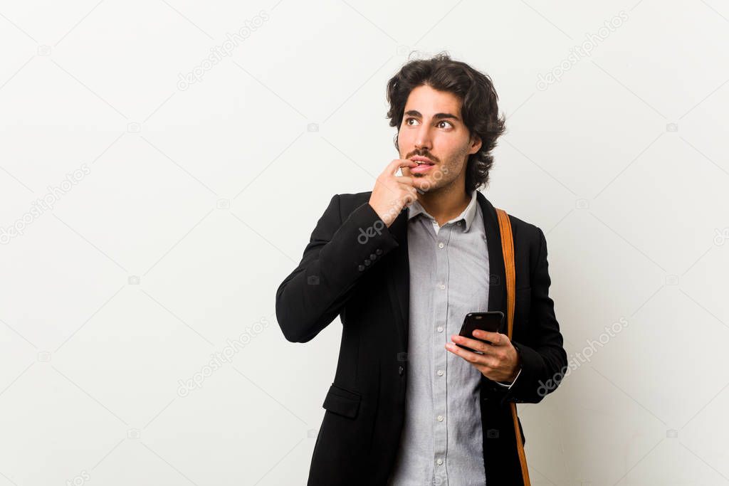 Young business man holding a phone relaxed thinking about something looking at a copy space.