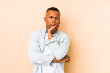 Bej arka planda izole edilmiş, sıkılmış, yorgun ve dinlenmeye ihtiyacı olan genç Latin bir adam..