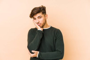 Bej bir arka planda izole edilmiş, sıkılmış, yorgun ve dinlenmeye ihtiyacı olan genç bir Arap adam..